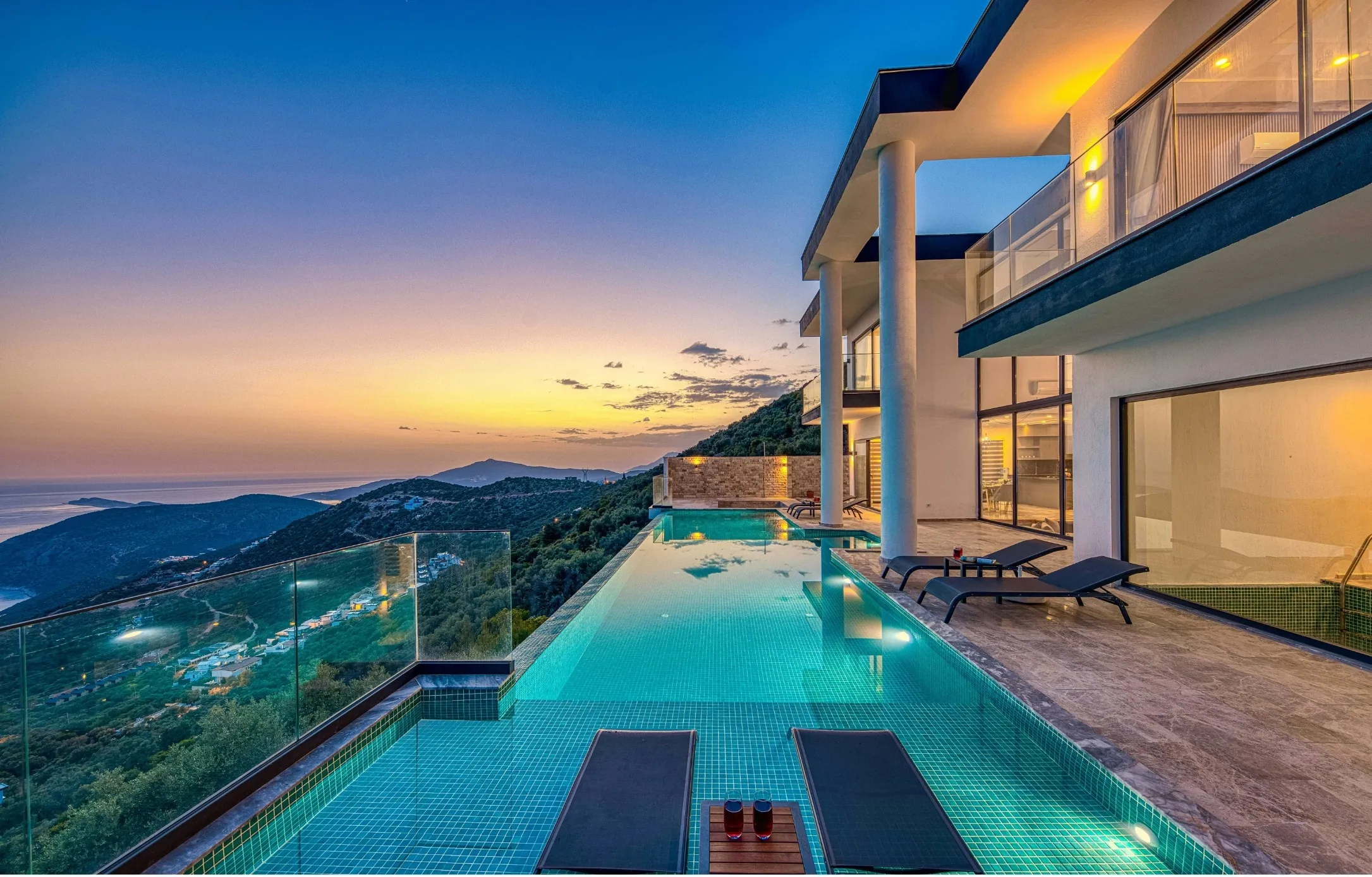 Hillside villa terrace with an infinity pool overlooking the water at sunset